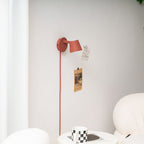 Red Clérachic wall light with its shade swung out to the side, notes pinned beside it and a mug on the table below.