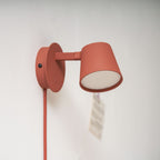 Close view of a red Clérachic wall light with a small round backplate, the shade facing out and a blurred note pinned nearby.