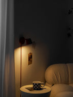 Red Clérachic wall light lit in a dim corner, its cord running down to a mug on a table beside a boucle sofa.