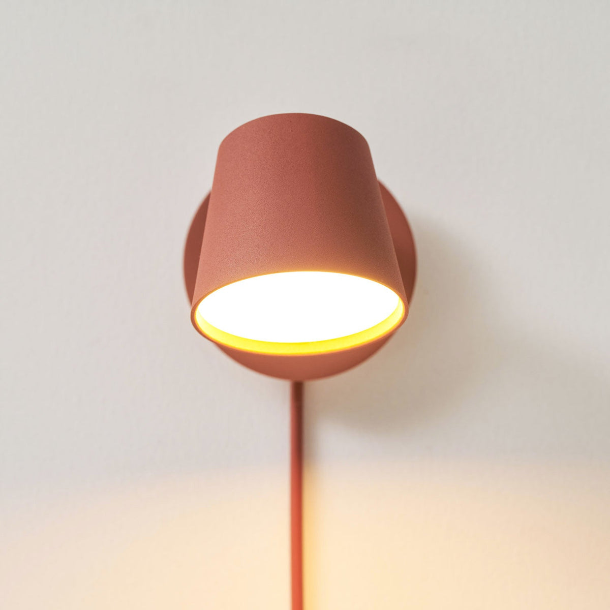 Close view of the glowing red Clérachic wall light, warm light showing under the tilted shade and the cord running below.