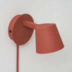 Close view of the arm, backplate and button on this red Clérachic wall light, with the cone shade angled to the right.