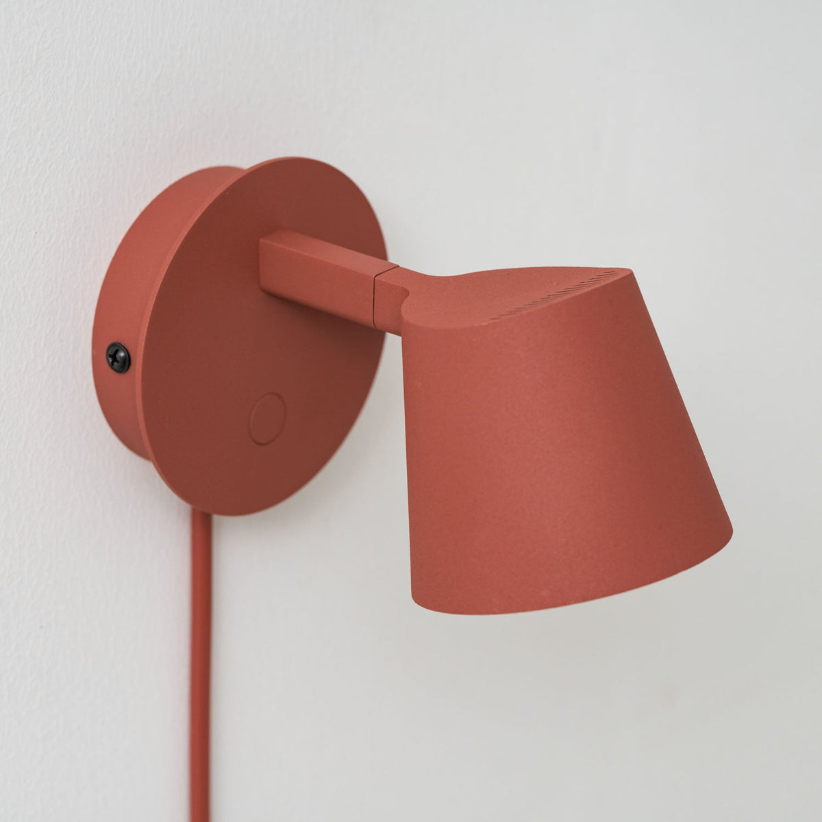 Close view of the arm, backplate and button on this red Clérachic wall light, with the cone shade angled to the right.