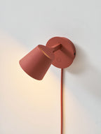 Red Clérachic wall light with the shade tilted up and sideways, throwing light along the wall behind it.