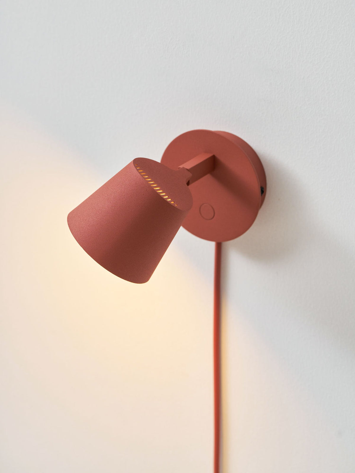 Red Clérachic wall light with the shade tilted up and sideways, throwing light along the wall behind it.