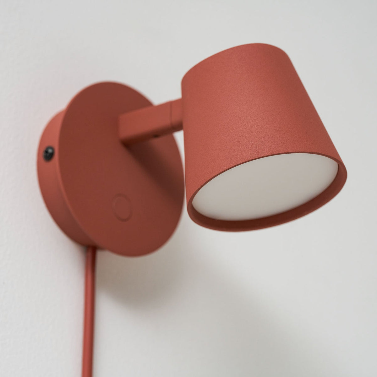 Close view of the red Clérachic wall light, its cone shade swung out on the arm with the diffuser facing the viewer.