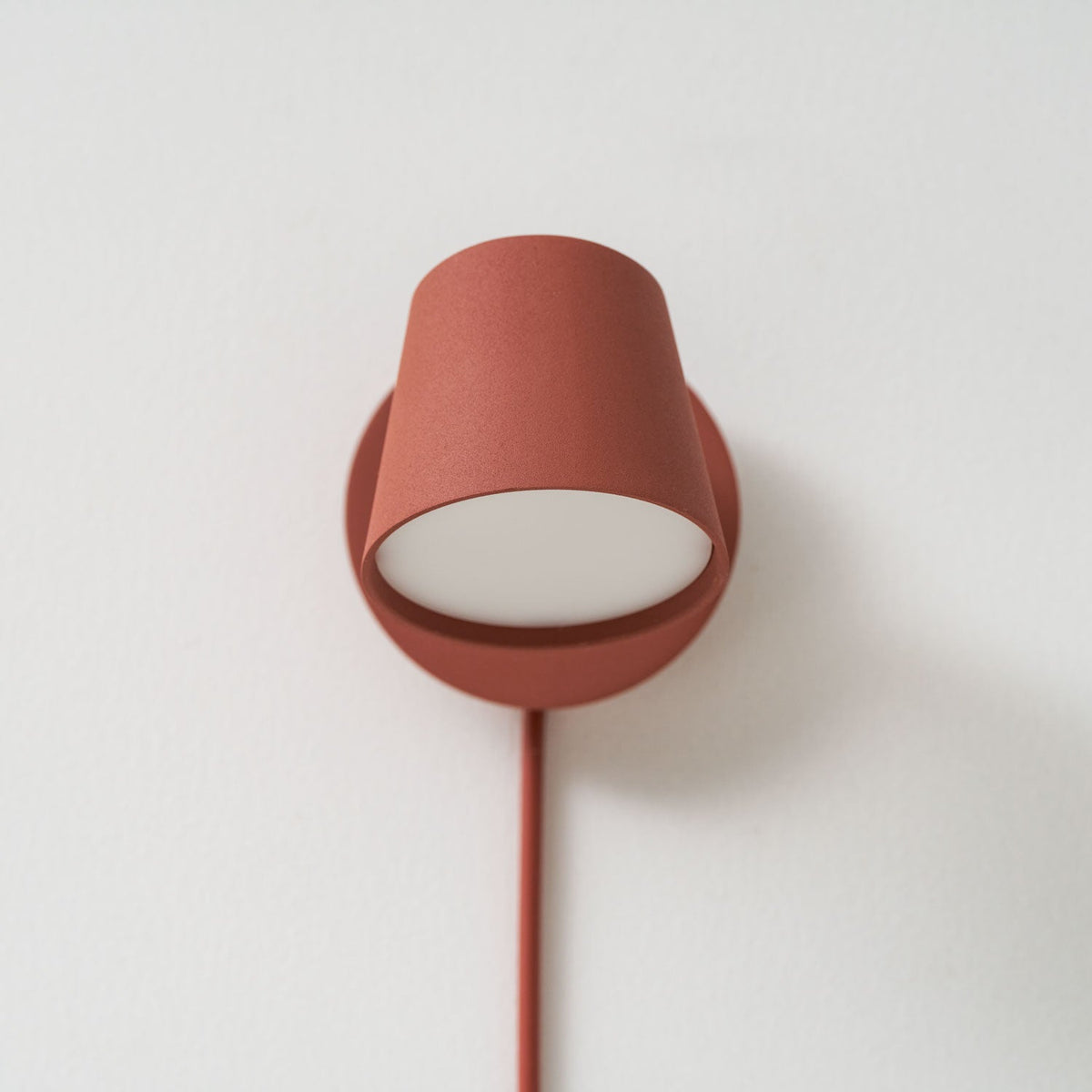 Red Clérachic wall light seen from the front, the cone shade turned down over the round backplate with a white diffuser.