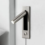 Round nickel head of this Clérachic wall light angled out from its plate, with a push button below, beside a white corner wall.