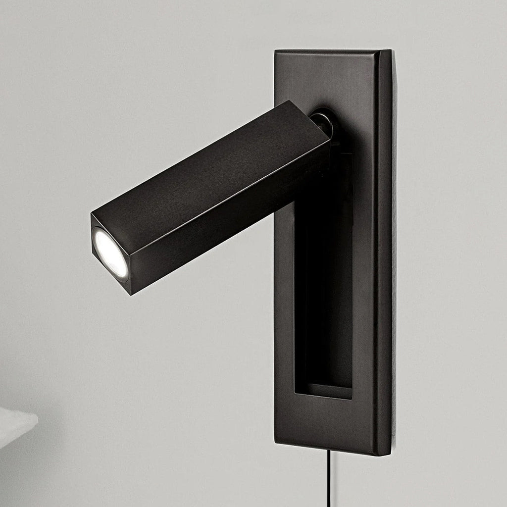 A square matt black head sits on a dark plate on this Clérachic wall light, angled out to the side on a grey wall.