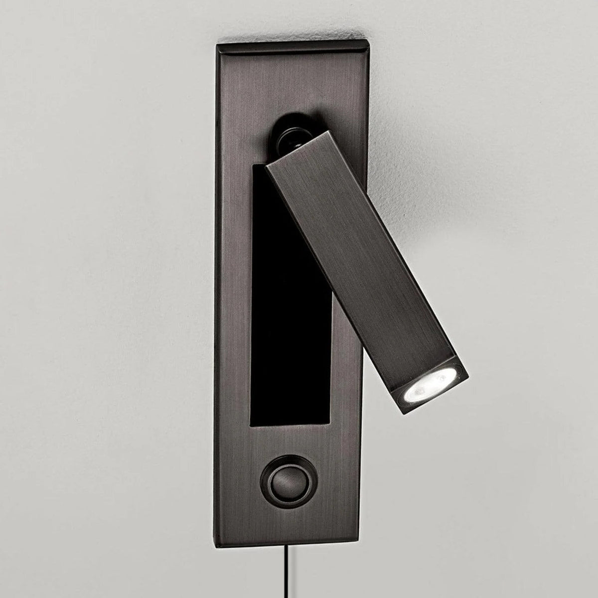 The head of this Clérachic wall light on a dark grey plate is swung diagonally downwards, with a round button below.