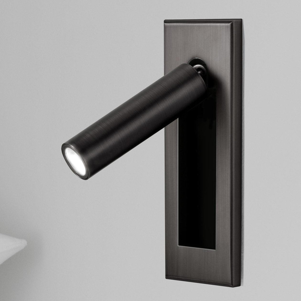 Matt black round head of this Clérachic wall light, angled out from a dark plate, with a pillow edge at the lower left.