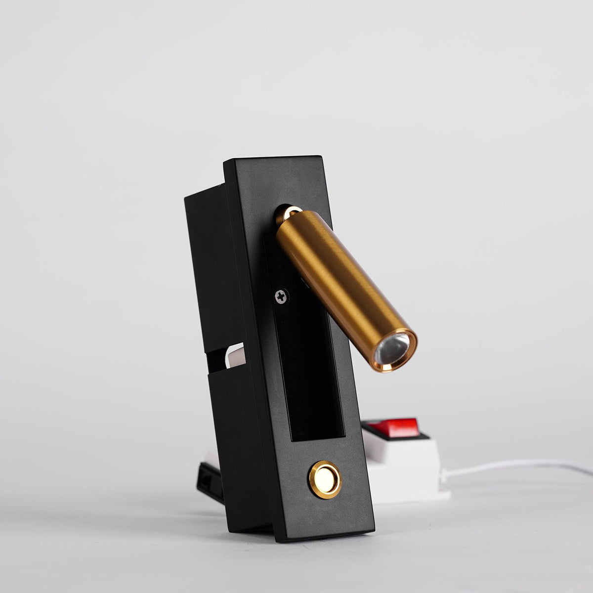Angled view of this Clérachic wall light with the brass-coloured head swung out, a round button below and a red switch behind.