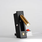This Clérachic wall light on a surface shows the brass-coloured head lit and angled right, with a power strip behind it.