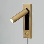 Brass-coloured round head and plate of this Clérachic wall light, lit and angled left, with a push button and cable below.