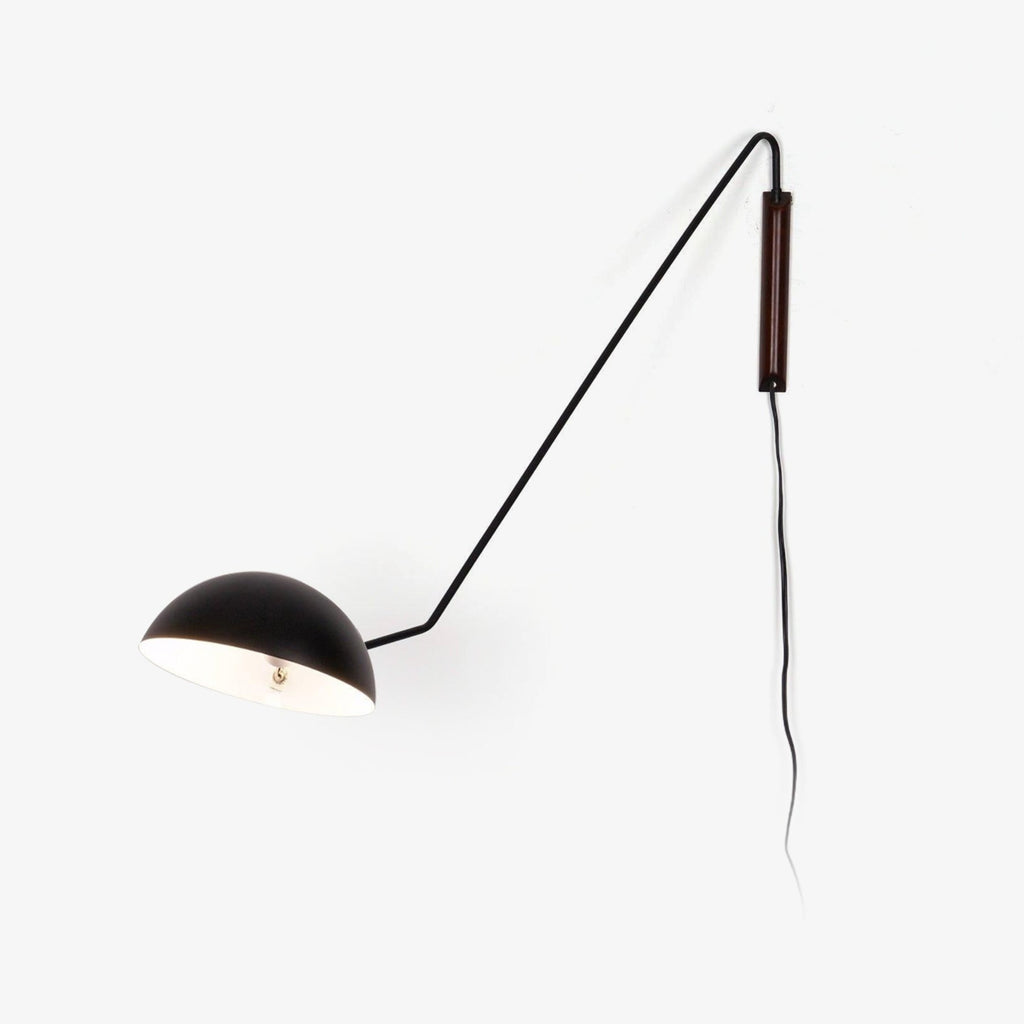 A black Clérachic wall light with a long swing arm, a half-dome shade and a walnut wall plate, on a plain white backdrop.