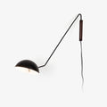 A black Clérachic wall light with a long swing arm, a half-dome shade and a walnut wall plate, on a plain white backdrop.