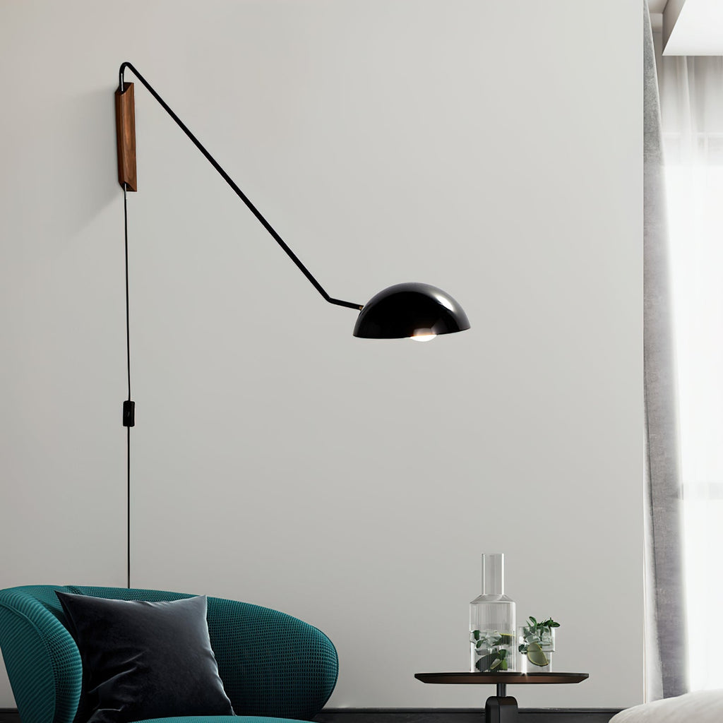 Black Clérachic pivoting wall light with a trailing cord and in-line switch, above a teal armchair and a glass carafe.