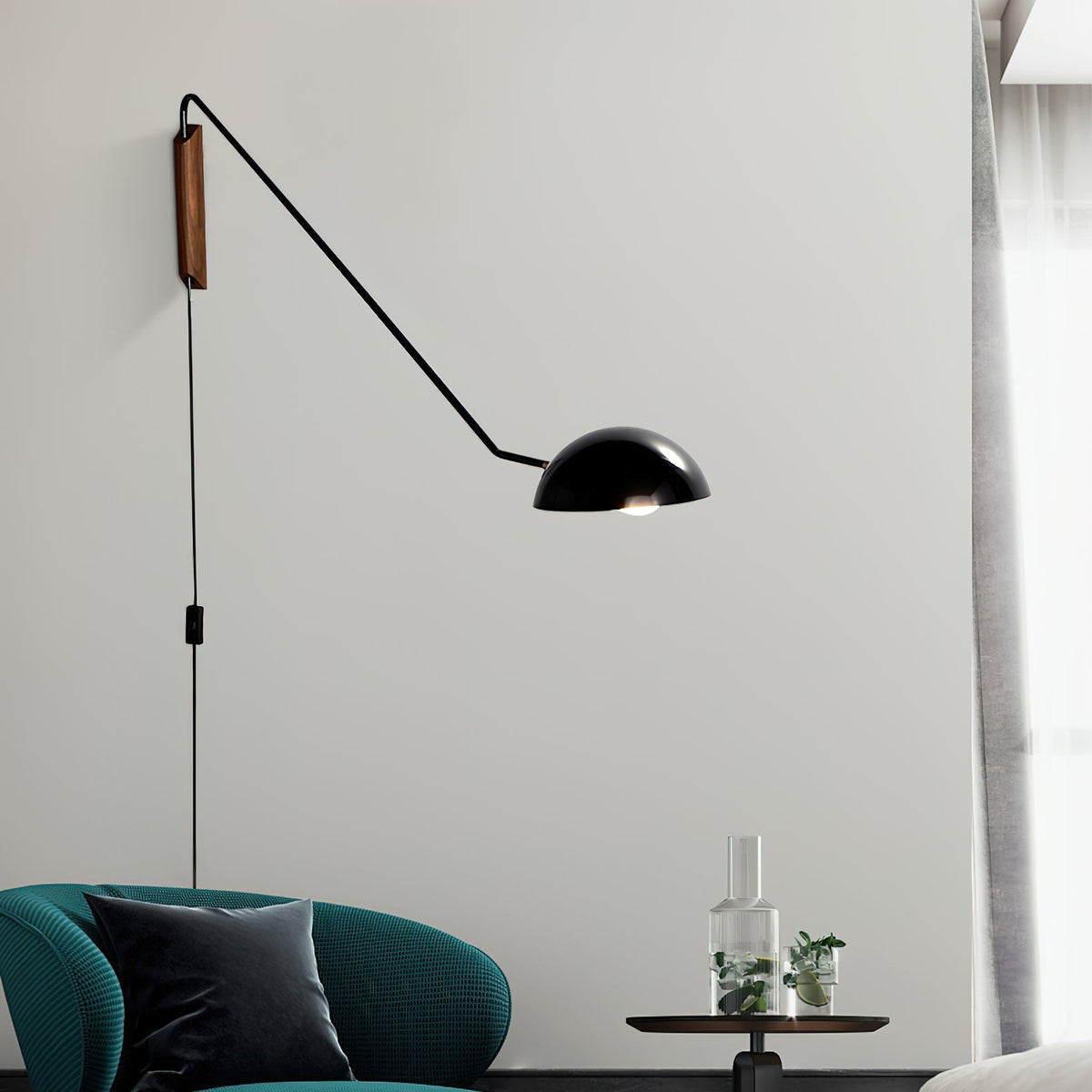 Black Clérachic pivoting wall light with a trailing cord and in-line switch, above a teal armchair and a glass carafe.