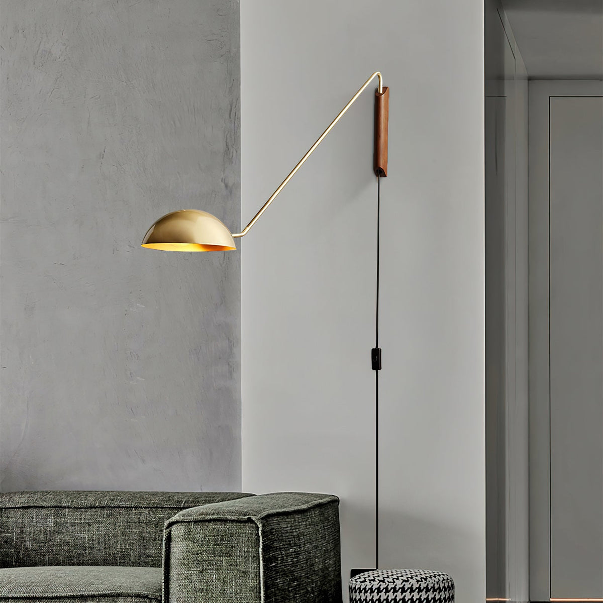 Gold and walnut Clérachic wall light on a grey plaster wall, with a dark green sofa below and a plain door behind.