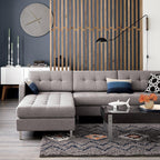 Black Clérachic wall light on a long arm beside a slatted wood divider, above a grey sectional sofa and a shaggy rug.