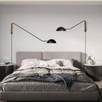 Two black Clérachic swing-arm wall lights flank a grey upholstered bed, one arm reaching further than the other.