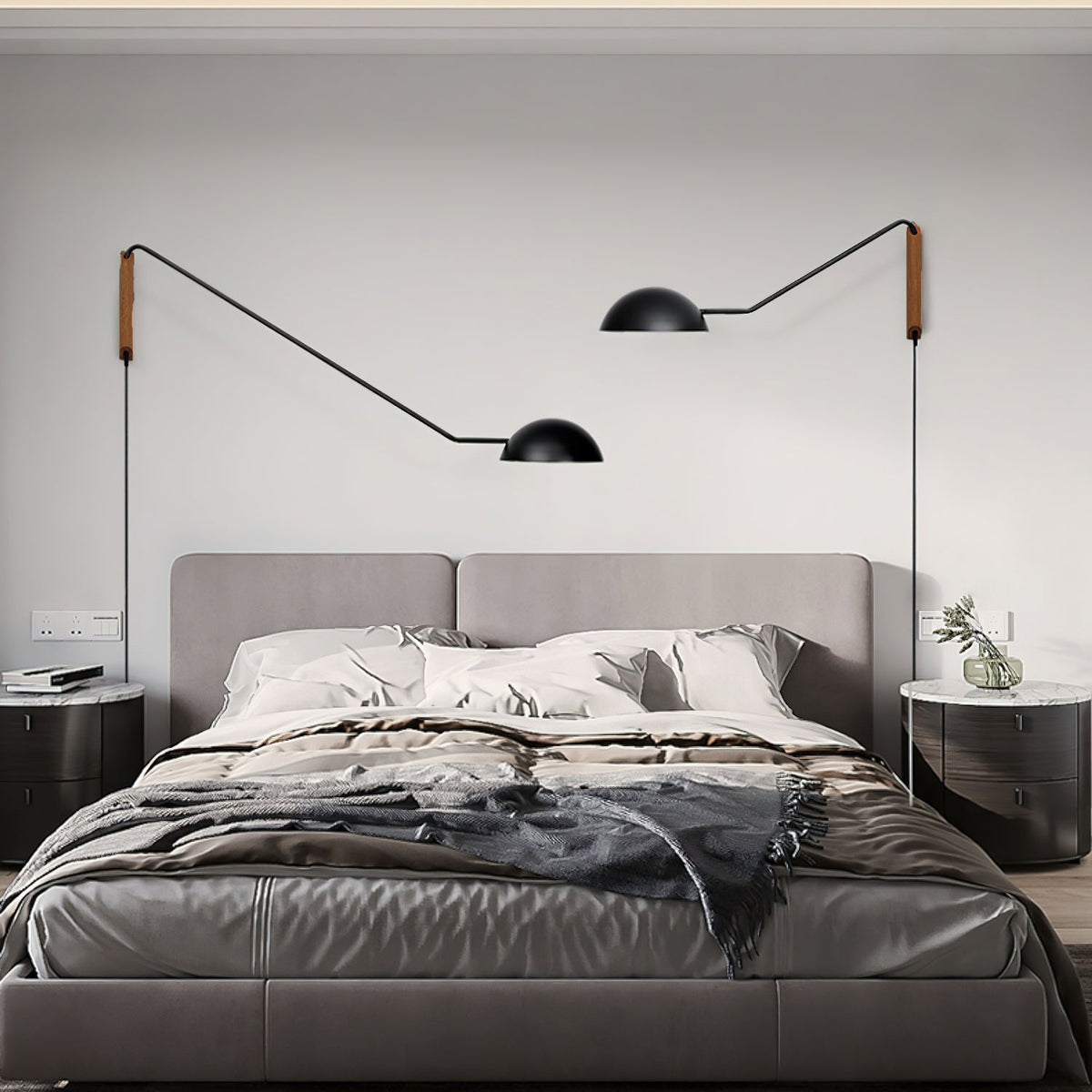 Two black Clérachic swing-arm wall lights flank a grey upholstered bed, one arm reaching further than the other.