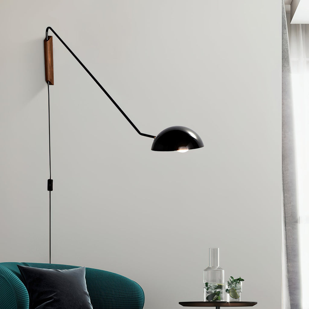 Close view of a black Clérachic wall light with a dome shade, above a teal armchair and a glass carafe on a side table.