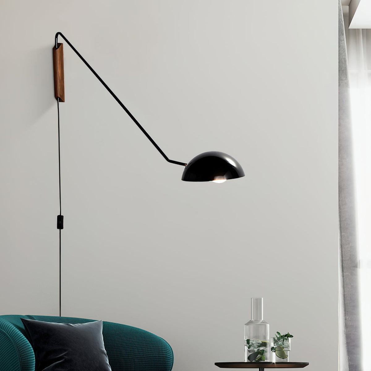 Close view of a black Clérachic wall light with a dome shade, above a teal armchair and a glass carafe on a side table.
