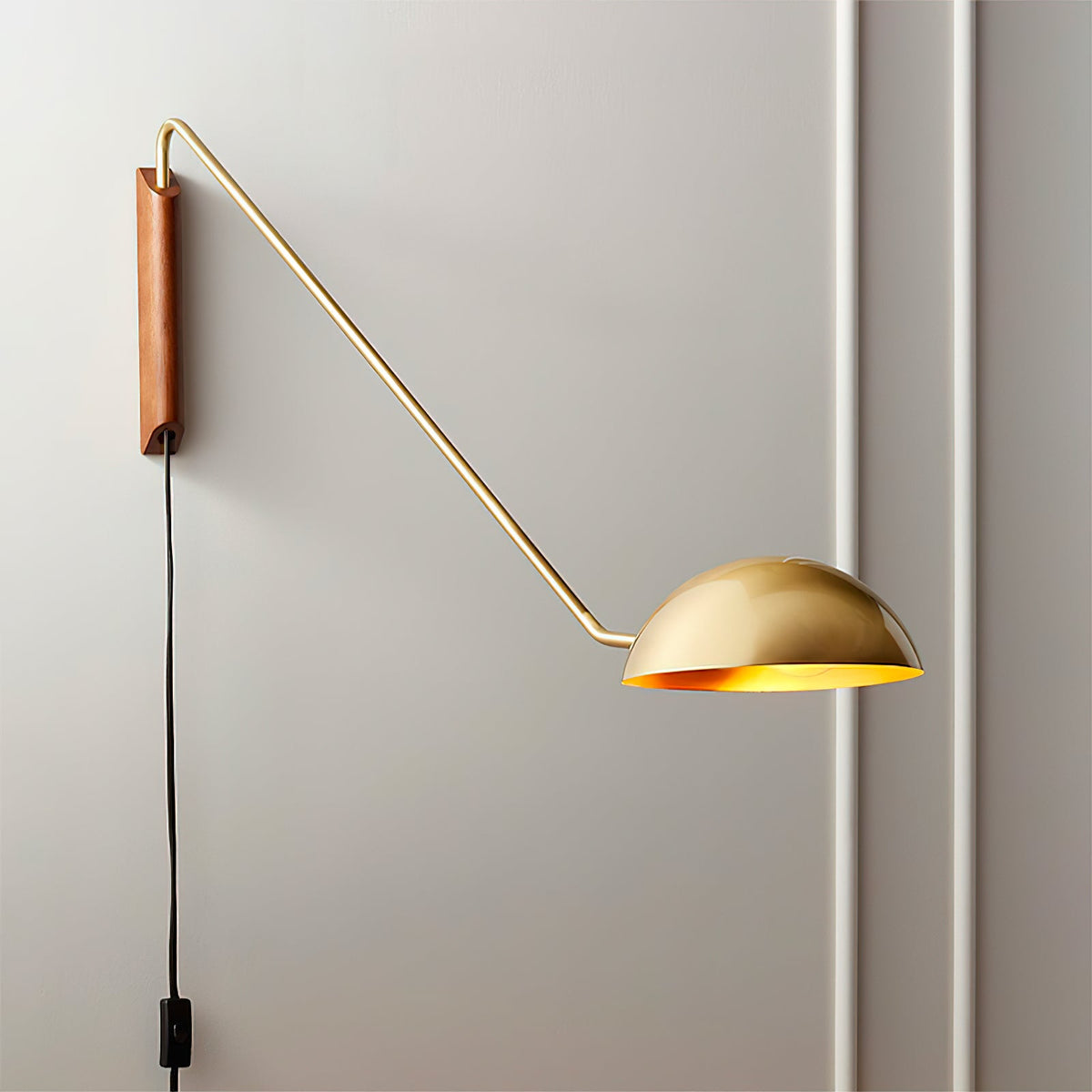 Close view of the brass-toned arm, walnut wall plate and dome shade of this Clérachic gold wall light, with its black cord below.