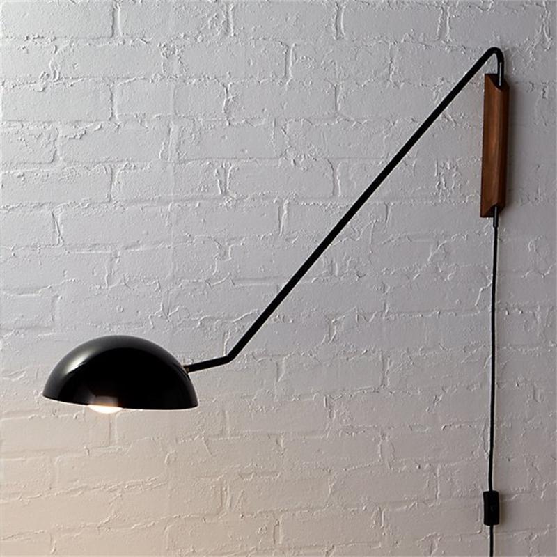 A black Clérachic wall light on a painted white brick wall, with its inner shade glowing and the cord hanging below.