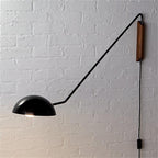 A black Clérachic wall light on a painted white brick wall, with its inner shade glowing and the cord hanging below.