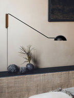 Black Clérachic wall light with a long arm over a dark ledge holding stones and a dried branch, against a warm beige wall.