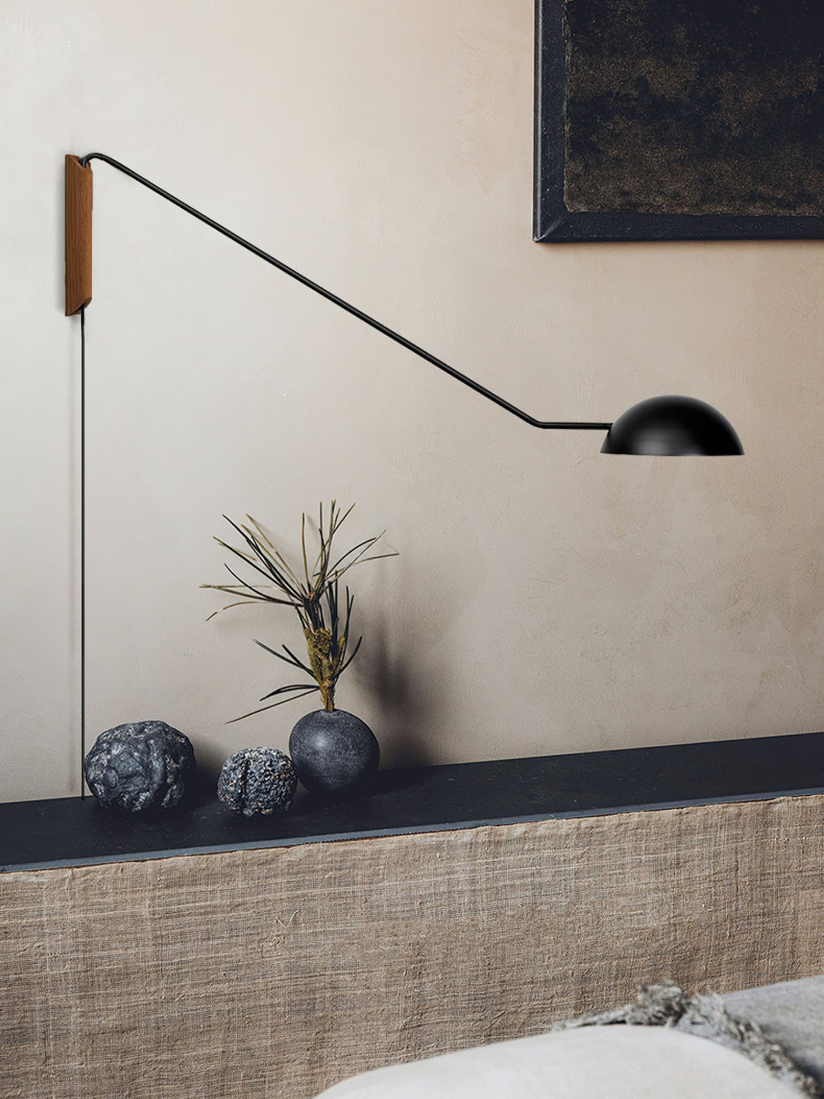 Black Clérachic wall light with a long arm over a dark ledge holding stones and a dried branch, against a warm beige wall.