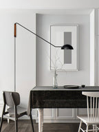 A black Clérachic wall light on a long arm above a dining table, beside a framed grey print and a glass vase of twigs.