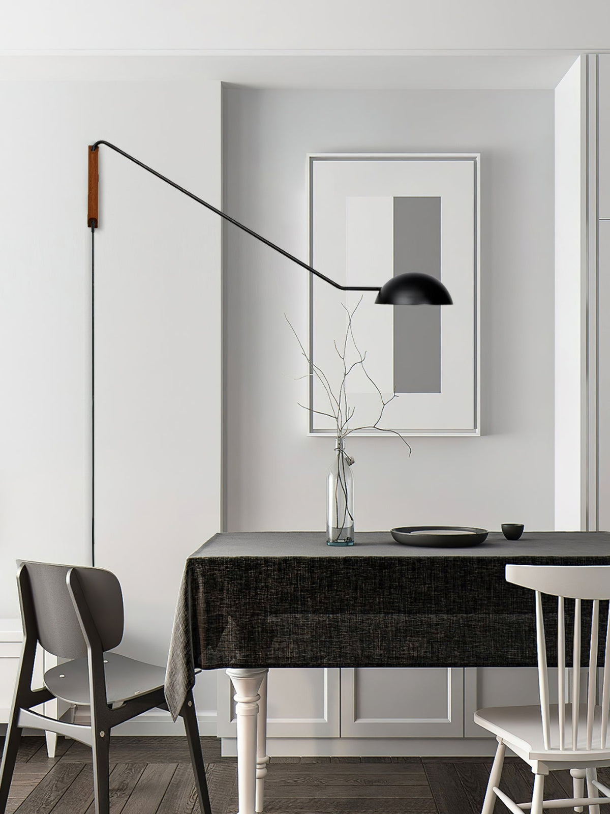A black Clérachic wall light on a long arm above a dining table, beside a framed grey print and a glass vase of twigs.