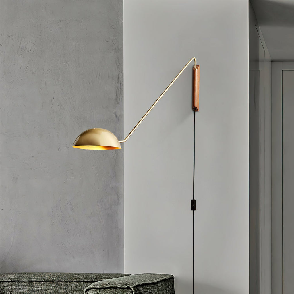 Gold and walnut Clérachic wall light on a grey plaster wall, with its black cord and switch hanging to a sofa below.