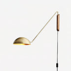 A gold and walnut Clérachic wall light with a thin arm and a half-dome shade, on a plain white backdrop.
