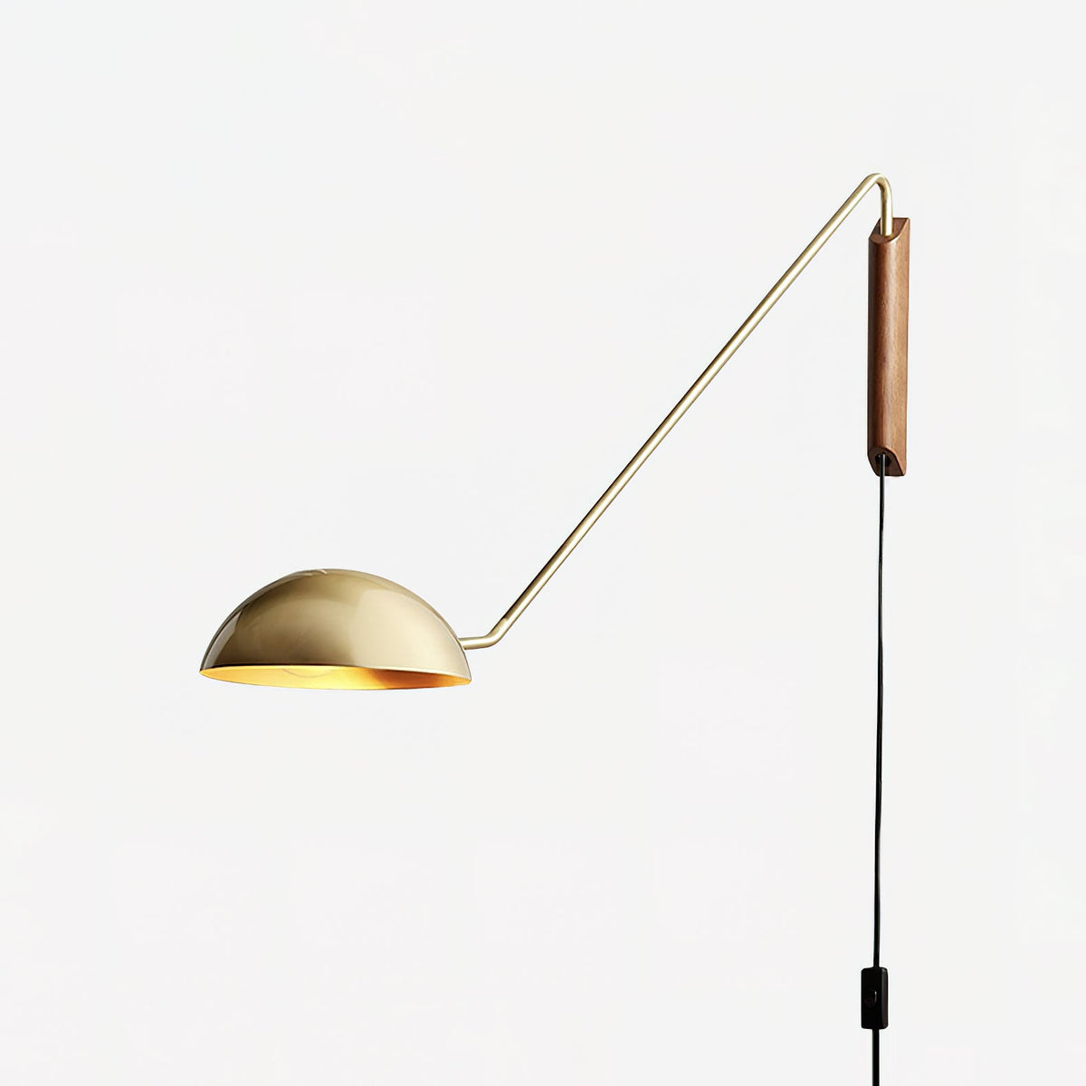 A gold and walnut Clérachic wall light with a thin arm and a half-dome shade, on a plain white backdrop.