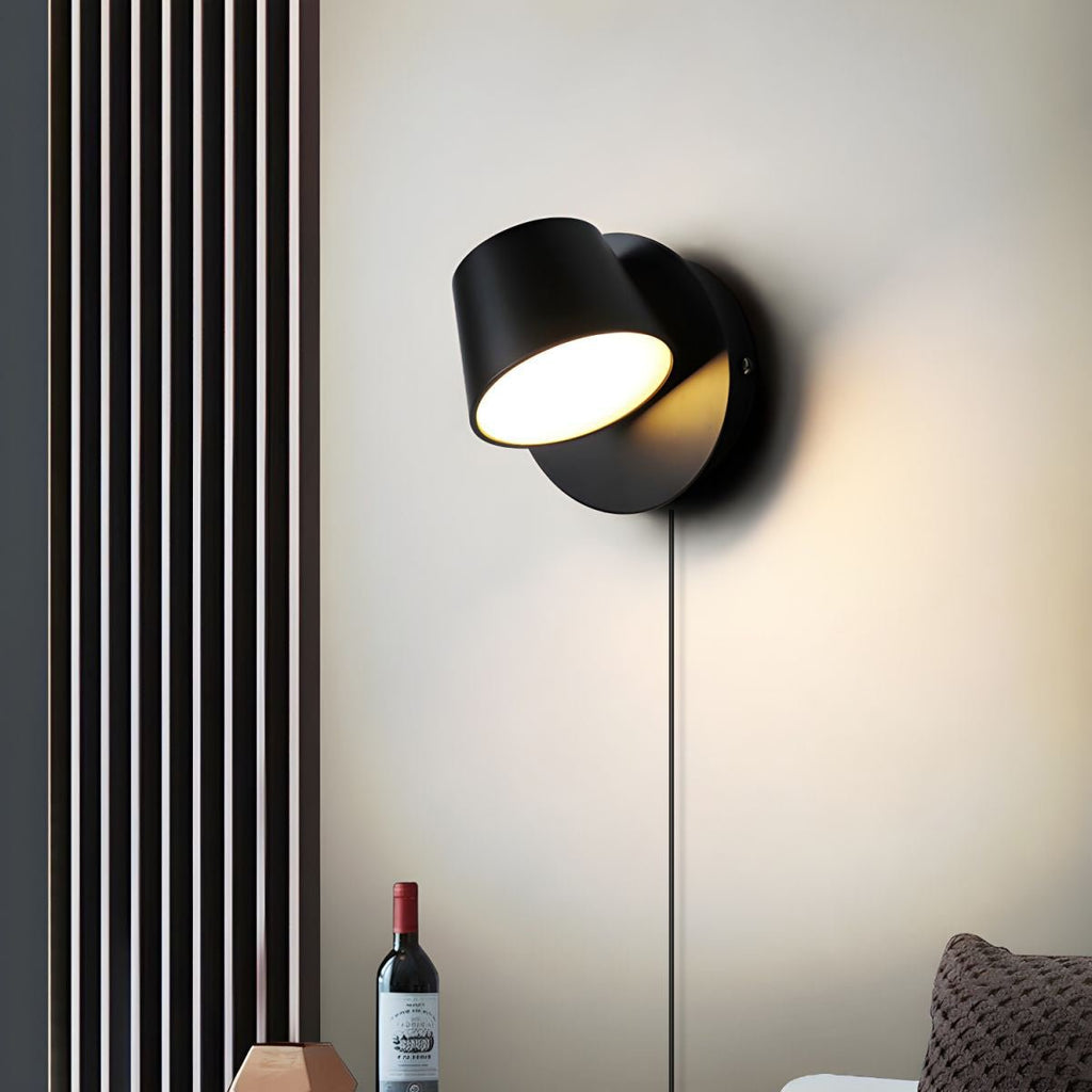 Single-light black Clérachic wall light turned to the side on a cream wall, beside a vertical slatted panel and a wine bottle.