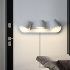 Three-light white Clérachic wall light on a grey wall beside a black door, the shades angled in different directions above a bed.