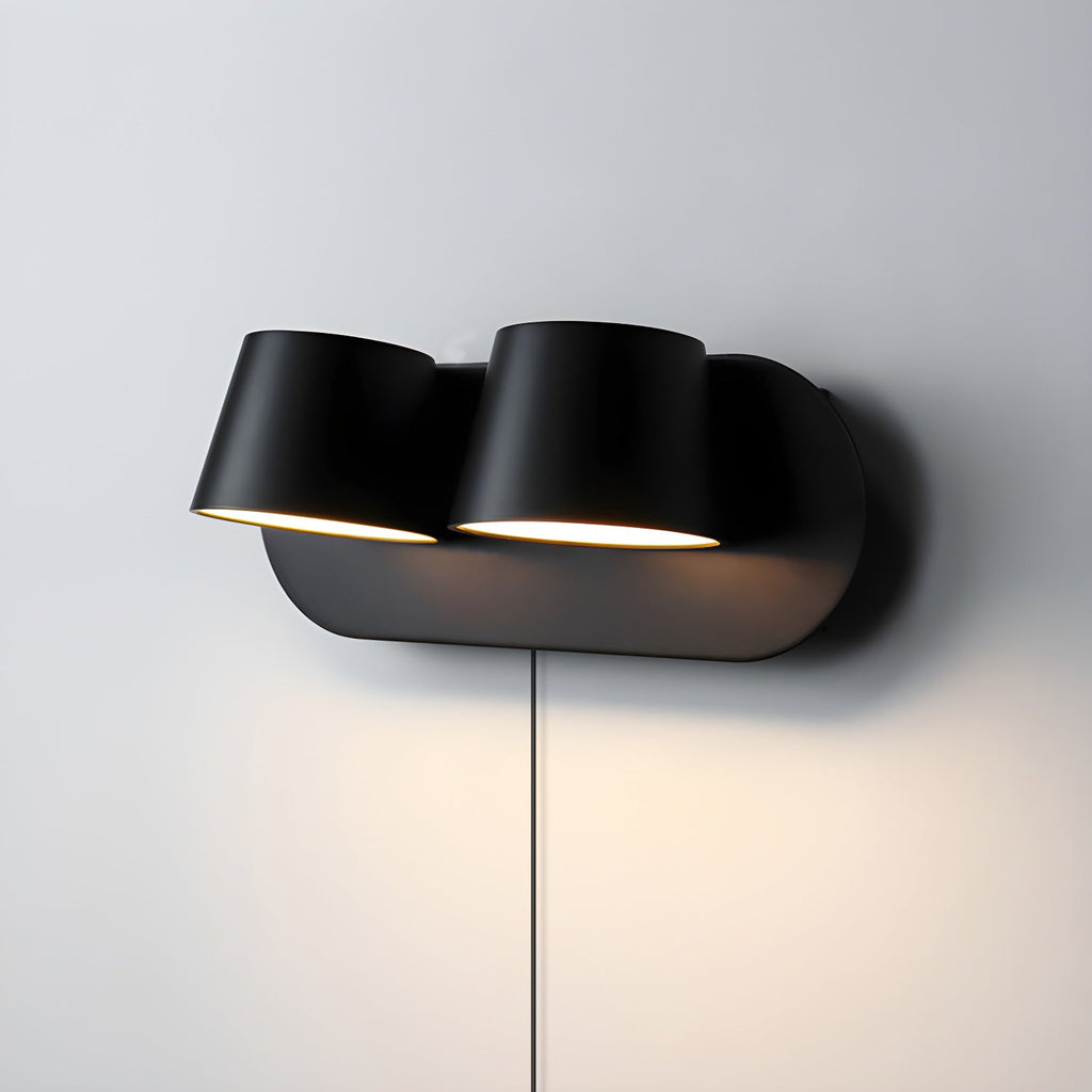 Two-light black Clérachic wall light on a pale grey wall, both shades lit and the black oval plate casting a soft shadow.