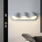 White Clérachic wall light with three shades above a bed corner, fixed beside a black door frame and lit warm on the wall.