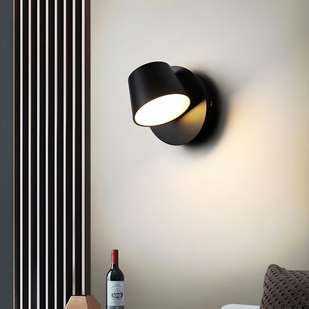 Black single-light Clérachic wall light on a cream wall beside a slatted panel, with a wine bottle and a woven cushion below.