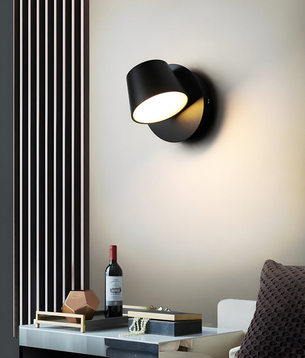 Black single-light Clérachic wall light on a cream wall beside a slatted panel, above a tray with a wine bottle and small ornaments.