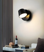Black single-light Clérachic wall light on a cream wall beside a slatted panel, above a tray with a wine bottle and small ornaments.