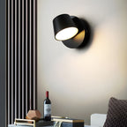 Black single-light Clérachic wall light with its head tilted to the left, set beside a slatted panel with a bottle and bowl beneath.