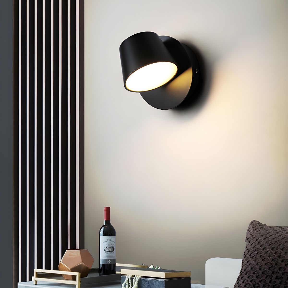 Black single-light Clérachic wall light with its head tilted to the left, set beside a slatted panel with a bottle and bowl beneath.
