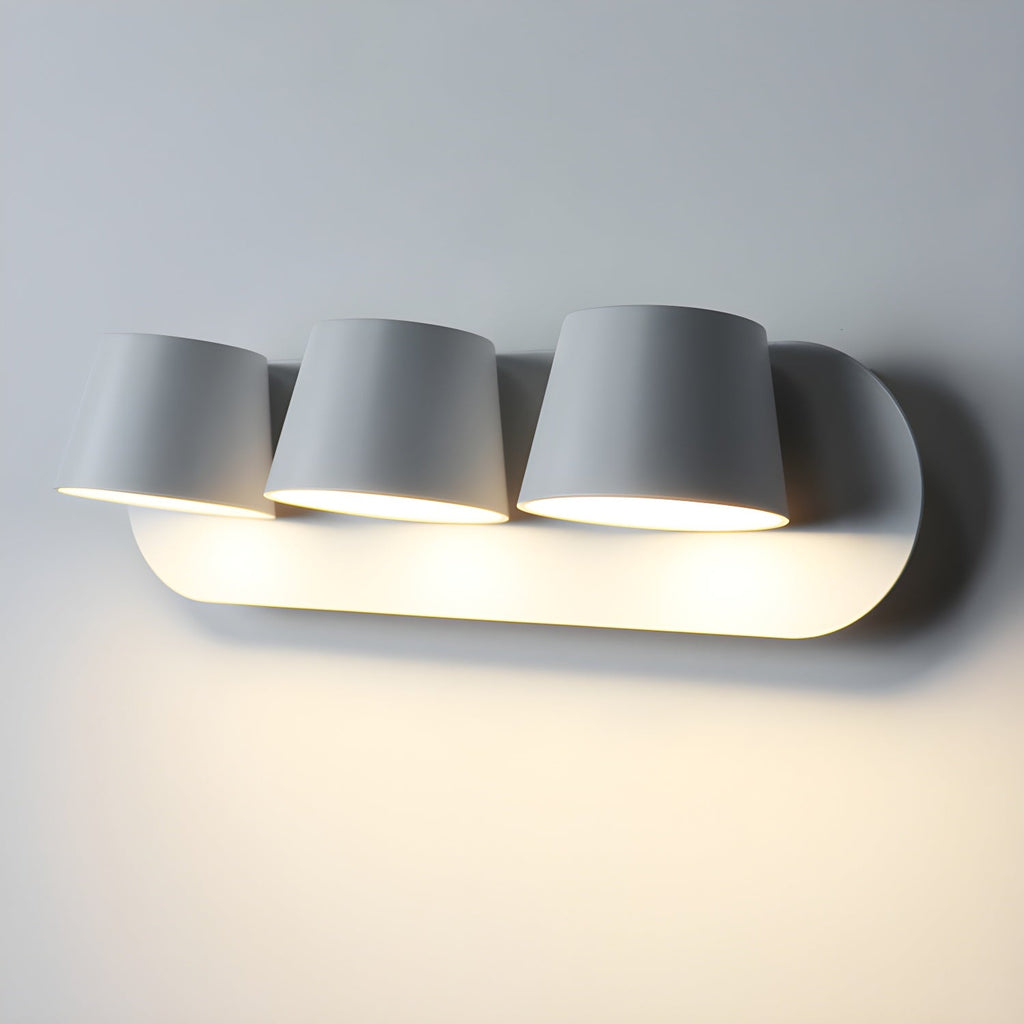 Close view of the three-light white Clérachic wall light, three tapered shades lit warm and lighting the wall beneath the oval plate.