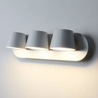 Close view of the three-light white Clérachic wall light, three tapered shades lit warm and lighting the wall beneath the oval plate.
