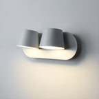 Close view of the two-light white Clérachic wall light, its tapered shades lit and washing the grey wall beneath with warm light.