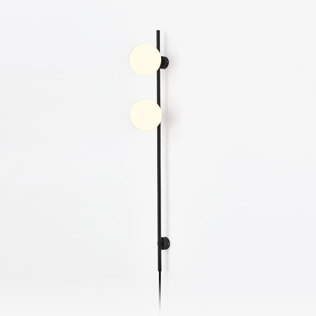 A Clérachic plug-in wall light with two frosted white globes on a slim black rod, with the cord trailing down a plain white wall.